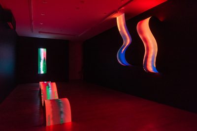 Installation photo of gallery, curly LED sculptures in foreground to the left and background